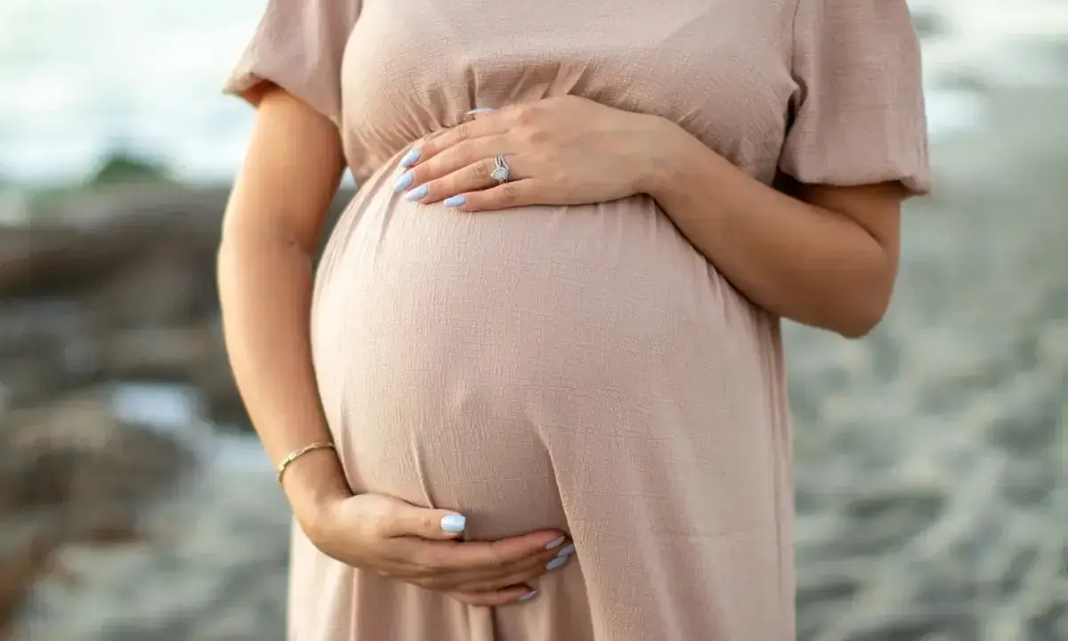 Brzuch kobiety w ciąży, delikatnie otulony dłonią. W trosce o zdrowie maluszka, przyszła mama unika kosmetyków z retinolem.
