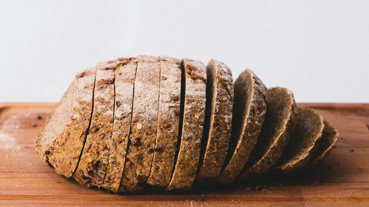 Pokrojony bochenek ciemnego chleba na desce. Zastanawiasz się, ile kcal ma kromka chleba?