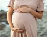 Brzuch kobiety w ciąży, delikatnie otulony dłonią. W trosce o zdrowie maluszka, przyszła mama unika kosmetyków z retinolem.