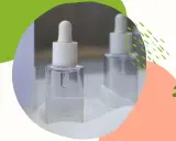 Szklane buteleczki z pipetką, zawierające serum z ethylhexylglycerin. Dwie buteleczki na białym tle, otoczone kolorowymi, abstrakcyjnymi kształtami.