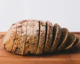 Pokrojony bochenek ciemnego chleba na desce. Zastanawiasz się, ile kcal ma kromka chleba?
