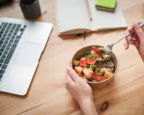 Ręce trzymające miskę z łososiem i warzywami, obok laptop i notatnik. Idealny posiłek na dieta okienkowa.