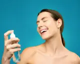 Uśmiechnięta kobieta rozpyla na twarz odświeżającą hydrolinę.
