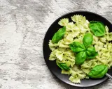 Lekkostrawny makaron farfalle z pesto i świeżą bazylią na czarnym talerzu, gotowy do podania.