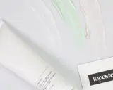 Biała tubka z kosmetykiem i kolorowe smugi kremów. Obok wizytówka z logo "topestetic", sugerująca znane marki kosmetyków.