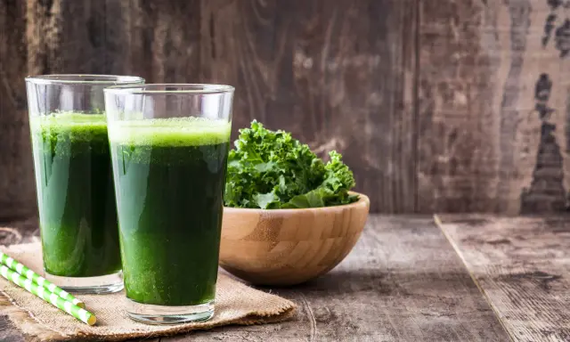 Dwa szklanki zielonego smoothie, miska jarmużu i słomki. Idealne na śniadanie zgodne z dietą sirtuinową.