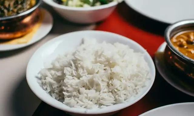 Biały ryż, źródło węglowodanów, w misce obok indyjskiego curry i sałatki.