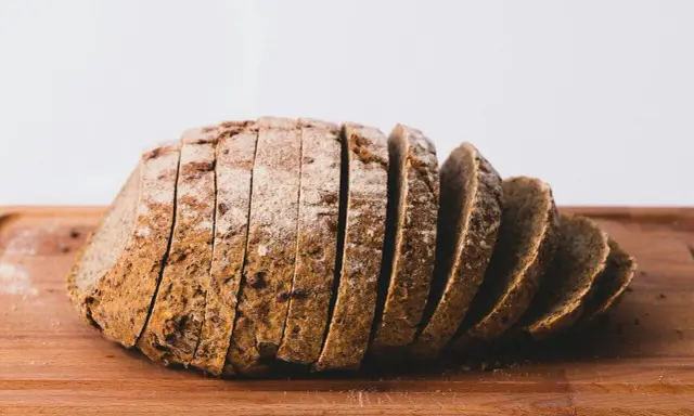 Pokrojony bochenek ciemnego chleba na desce. Zastanawiasz się, ile kcal ma kromka chleba?