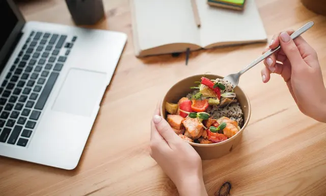 Ręce trzymające miskę z łososiem i warzywami, obok laptop i notatnik. Idealny posiłek na dieta okienkowa.