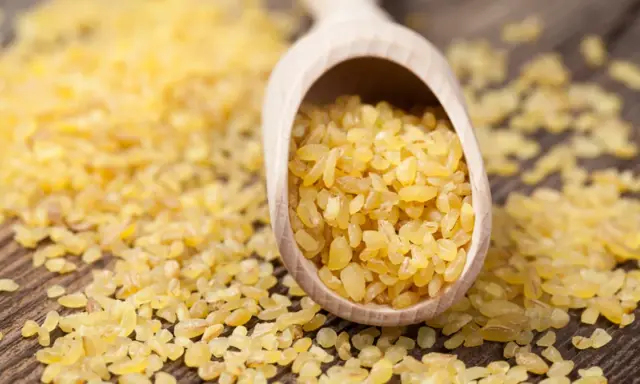 Kasza bulgur na drewnianej łyżce. Niska kasza bulgur indeks glikemiczny sprawia, że jest idealna dla diabetyków.