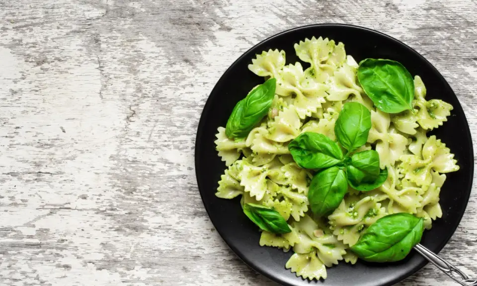 Lekkostrawny makaron farfalle z pesto i świeżą bazylią na czarnym talerzu, gotowy do podania.