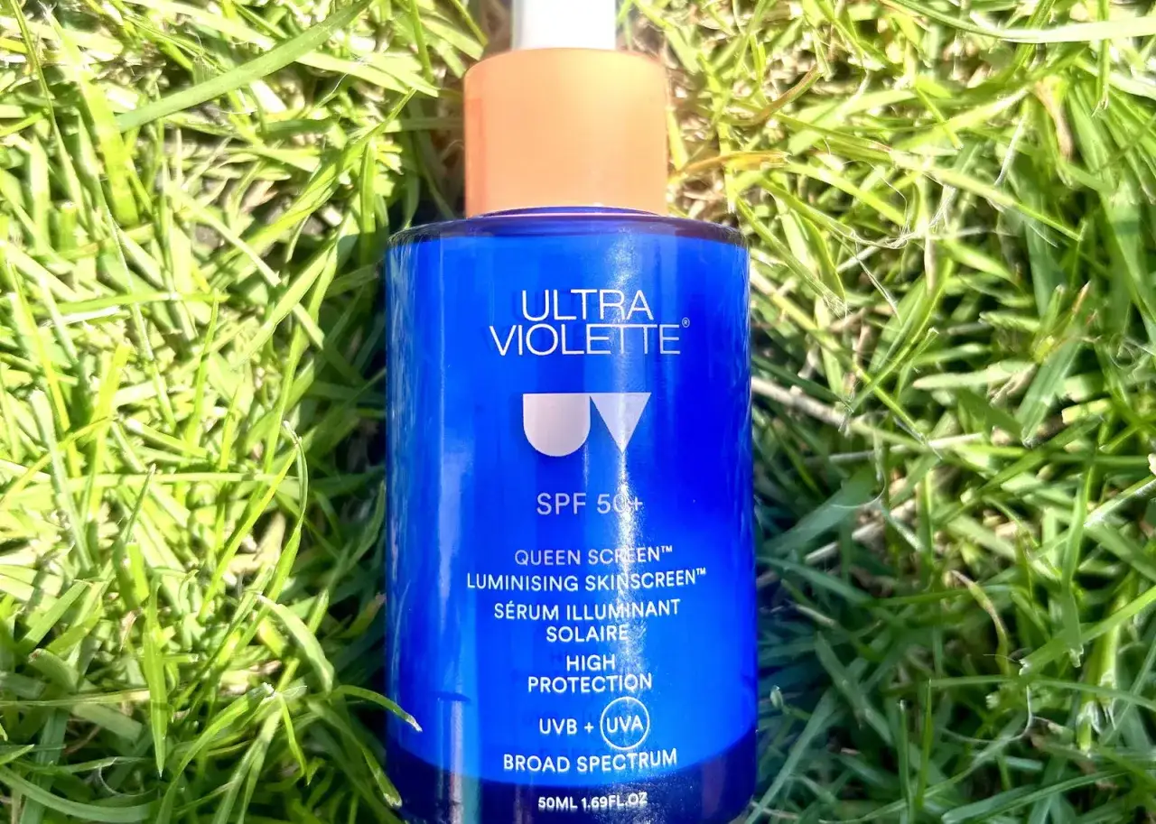 Niebieska butelka kremu z filtrem SPF 50+ Ultra Violette Queen Screen, który nadaje skórze promienny glow, leży na zielonej trawie.
