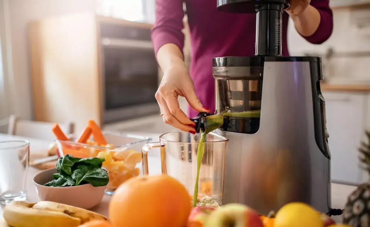 Kobieta przygotowuje świeży sok, rozpoczynając swoją przygodę z dietą sokową. Na stole owoce i warzywa.
